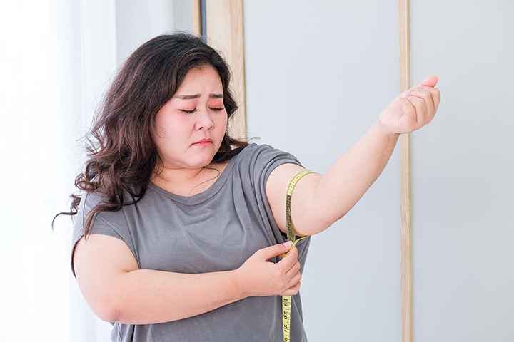 A fat Asian lady measuring the circumference of her arm with a measuring tape