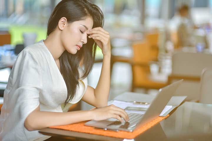 Woman closing her eyes as she sits in front of a laptop