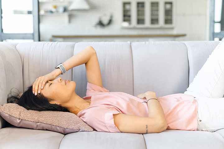 A woman lying down on the sofa while holding her stomach and forehead