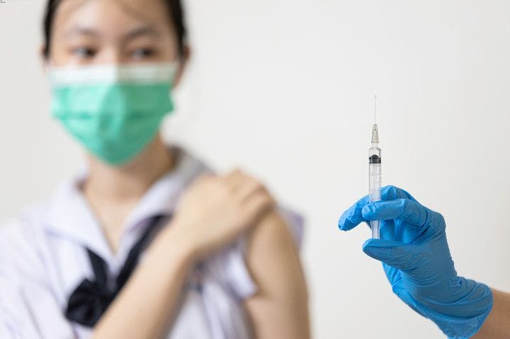 Doctor with a glove on right hand holding a syringe upright as a woman folds up her left sleeve in the background