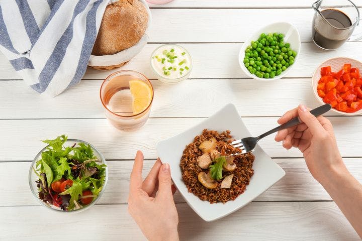 An overhead shot of a woman’s hands on a plate of brown rice with bowls of vegetables around it.