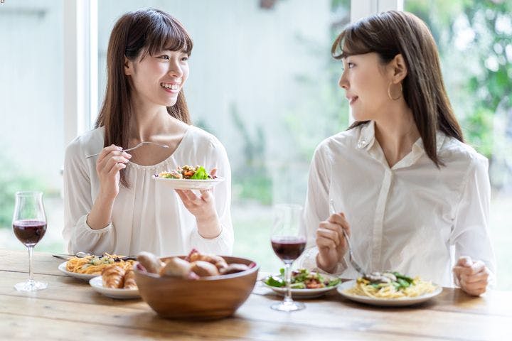 Two women eating lunch while chatting and drinking red wine together