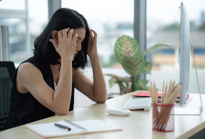 The side view of a female employee holding her head in frustration while sitting in front of her computer at work