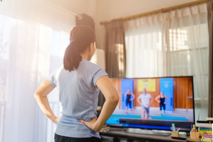 The back of a woman watching and imitating an exercise video on TV.