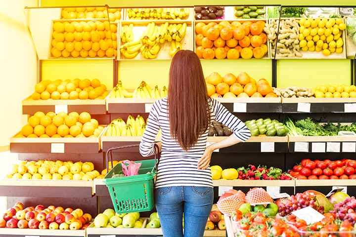 Woman holds shopping basket while looking at fresh produce in the supermarket