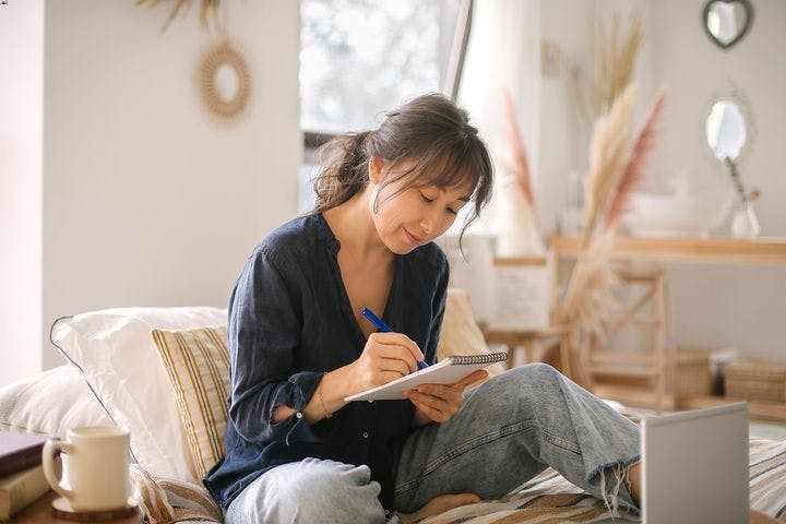 A woman sitting on a bed while writing on her journal