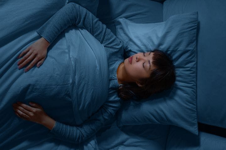 Woman sleeping on a blue-coloured pillow and covered with a duvet of the same colour