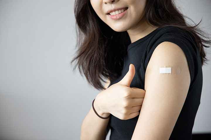 Smiling woman giving a thumbs up as she shows off her vaccination spot that’s covered with a plaster on her left arm.