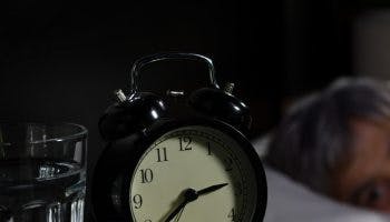 Elderly woman lying on the bed with eyes wide open at 2.40 am; the bedside table has a clock and some medication on it