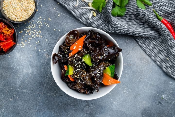 A meal prepared with black fungus, cucumber and carrots and garnished with sesame seeds in a white bowl
