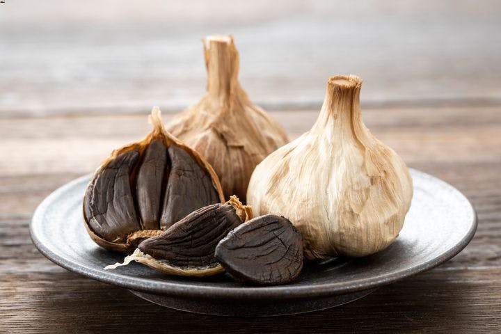 Black garlic on a ceramic plate that’s placed on a wooden table
