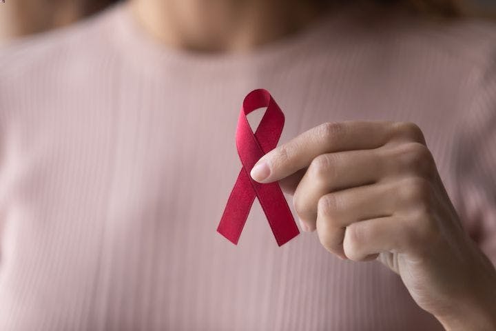 A close-up on a female hand holding a small red ribbon for HIV awareness.