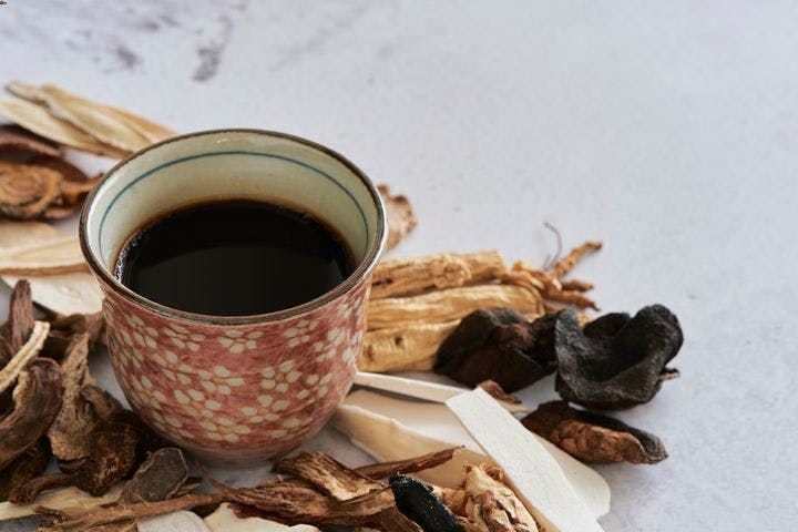 A cup of dark liquid surrounded by dried herbs