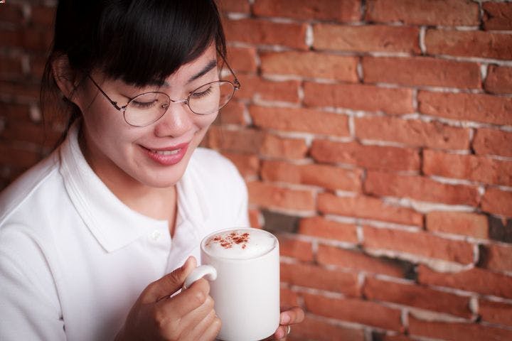 A woman holding a cup of foamy coffee sprinkled with cinnamon powder