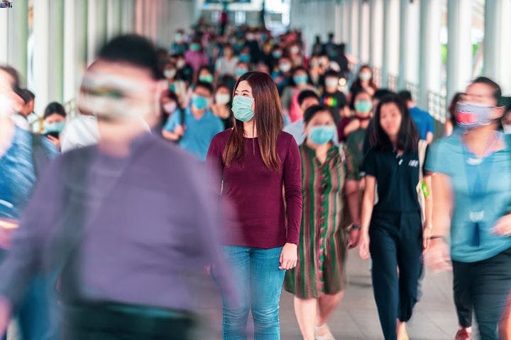 A woman wearing a mask and standing alone among a moving crowd