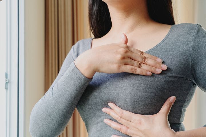 Woman in grey shirt examines one of her breasts with both hands