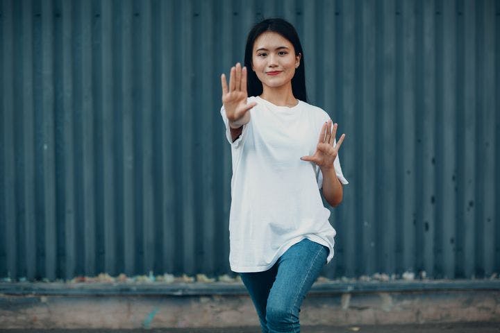 A young woman performing a Qigong move in a loose white T-shirt and denim.