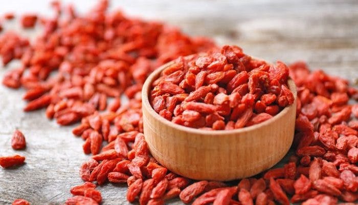 A small bowl of goji berries surrounded by pieces of scattered goji berries.