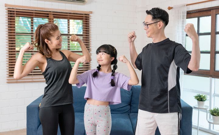 Parents and their daughter standing next to each other while flexing their arms.