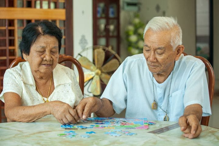 An elderly man and woman piecing together a jigsaw puzzle on a table