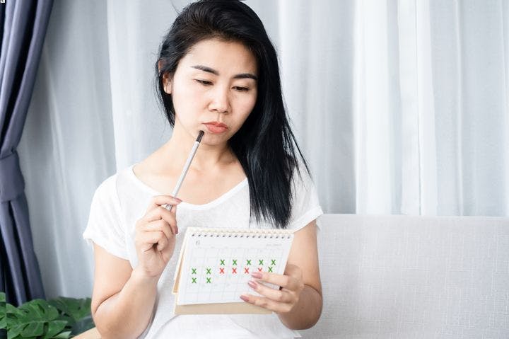 Woman staring at calendar noting her menstrual cycle.