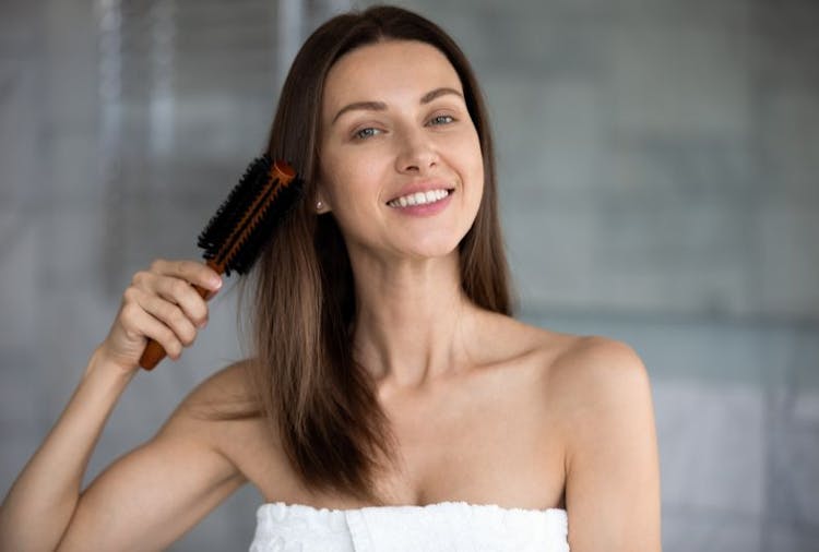 Woman smiling as she brushes her hair with a soft-bristle brush