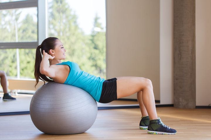 Woman performing a core exercise on a grey medicine ball in the gym