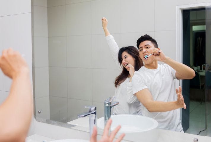 A man and woman brushing their teeth while dancing in front of a mirror