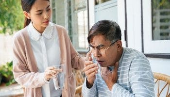 Older man coughing while younger woman offers glass of water