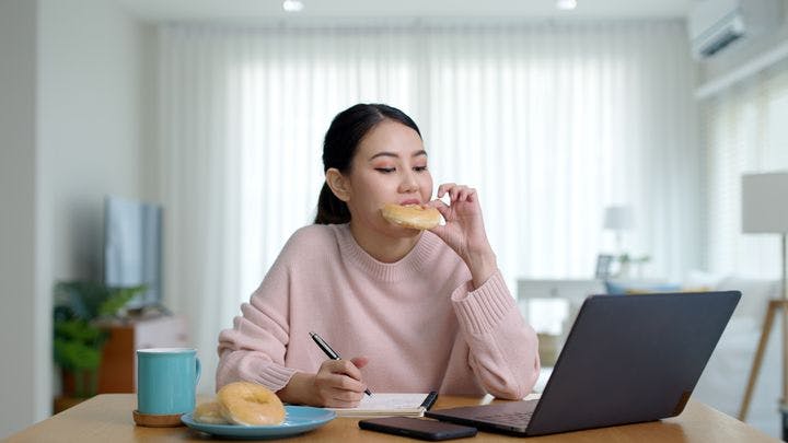 Young woman eating a doughnut while trying to work