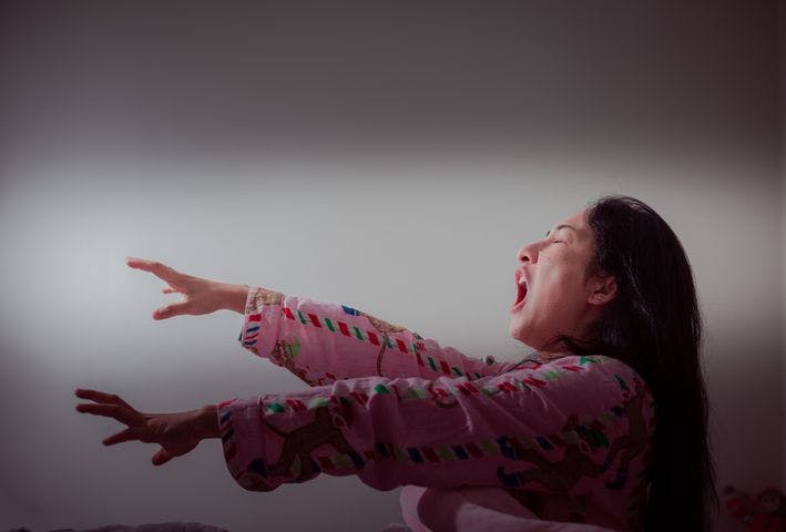 Woman yawning while extending hands out as she awakes from bed with her eyes closed