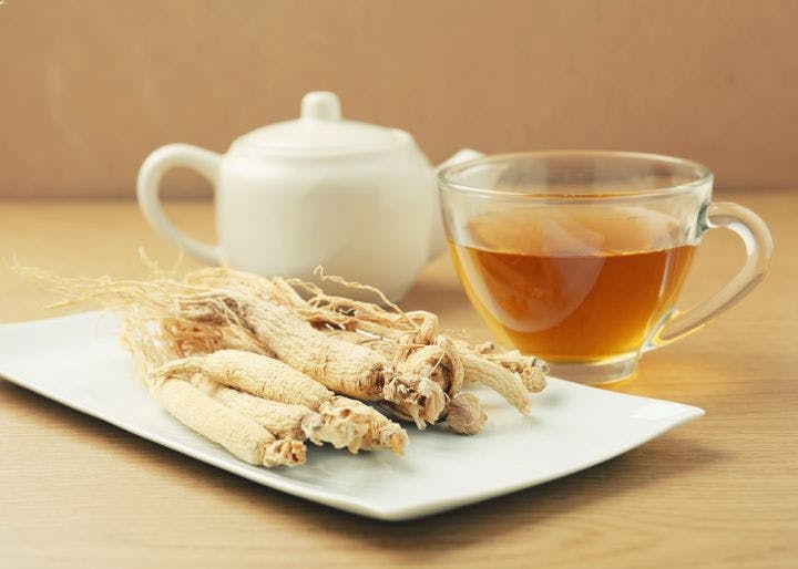Dried American ginseng root on a plate next to a cup of tea and teapot