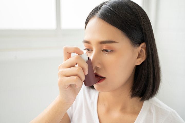 Woman placing an inhaler to her mouth using her right hand 