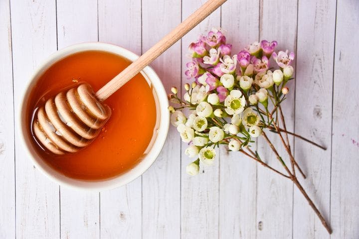An aerial view of a bowl of honey and Manuka flowers beside it.