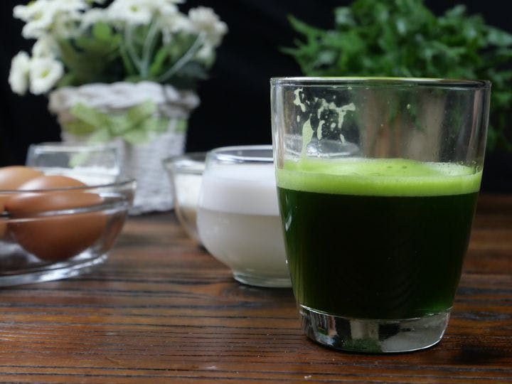 A glass of pandan leaf extract displayed with a bowl of eggs and other ingredients on a wooden table