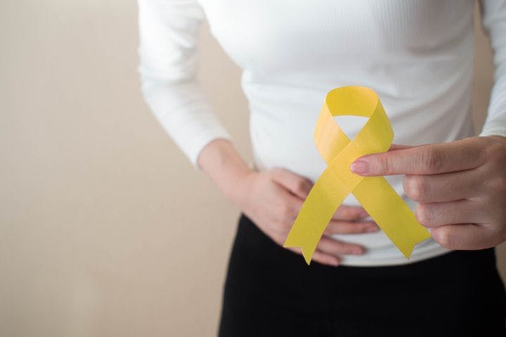 A partial view of a woman holding her stomach with one hand and a yellow ribbon in her other hand.