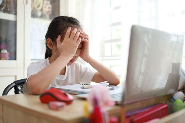 A young girl sitting at her desk in front of her laptop while burying her head in her hand