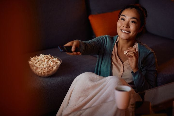 A woman eating popcorn while holding a remote control.