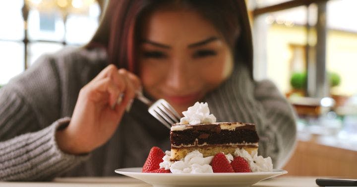 Woman poking a piece of cake with a fork as she looks at it, smiling 