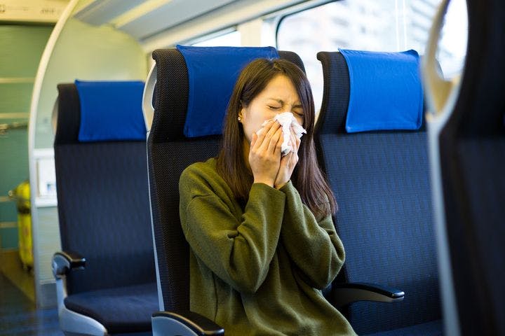 A woman sitting on a train while blowing her nose.