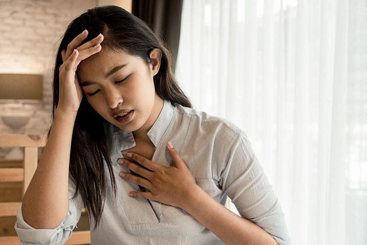 Woman struggling to breathe while holding her chest with her left hand and head with her right