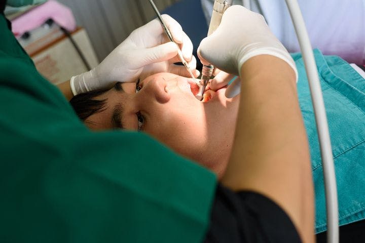 Dentist performing a dental procedure on a boy who’s looking up while lying down on a chair 