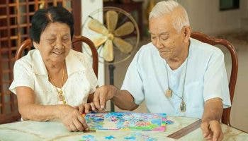 An elderly man and woman working on a jigsaw puzzle together as they sit at a table