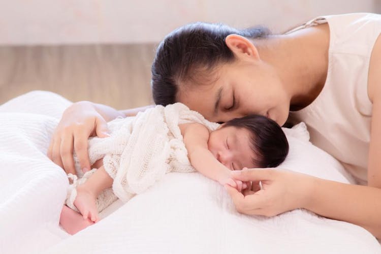 An Asian mother sleeping while holding her newborn baby