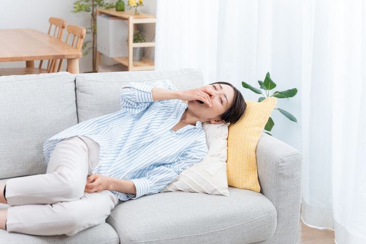 A woman lying sideways on the sofa while covering her yawn.