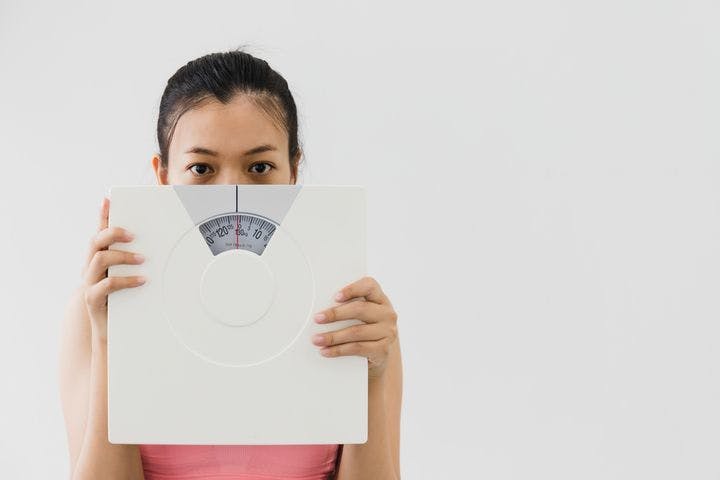 A woman covering half of her face with a weight scale.