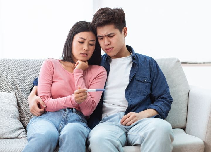 Young Asian couple sitting on a sofa with a pregnancy test in hand