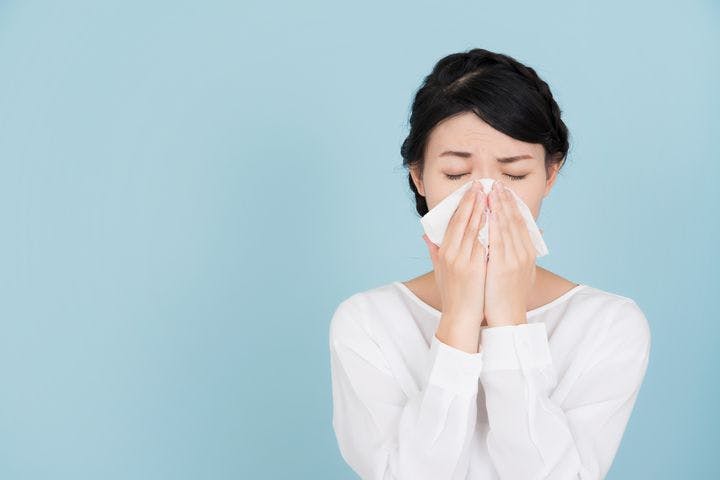 Woman sneezing into a piece of tissue with her eyes closed