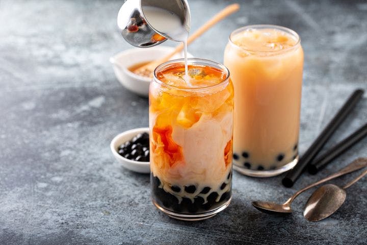 Two glasses of boba tea with straws and spoons on a grey surface