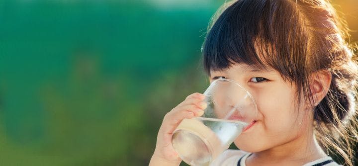 A young Asian girl drinking water from her glass